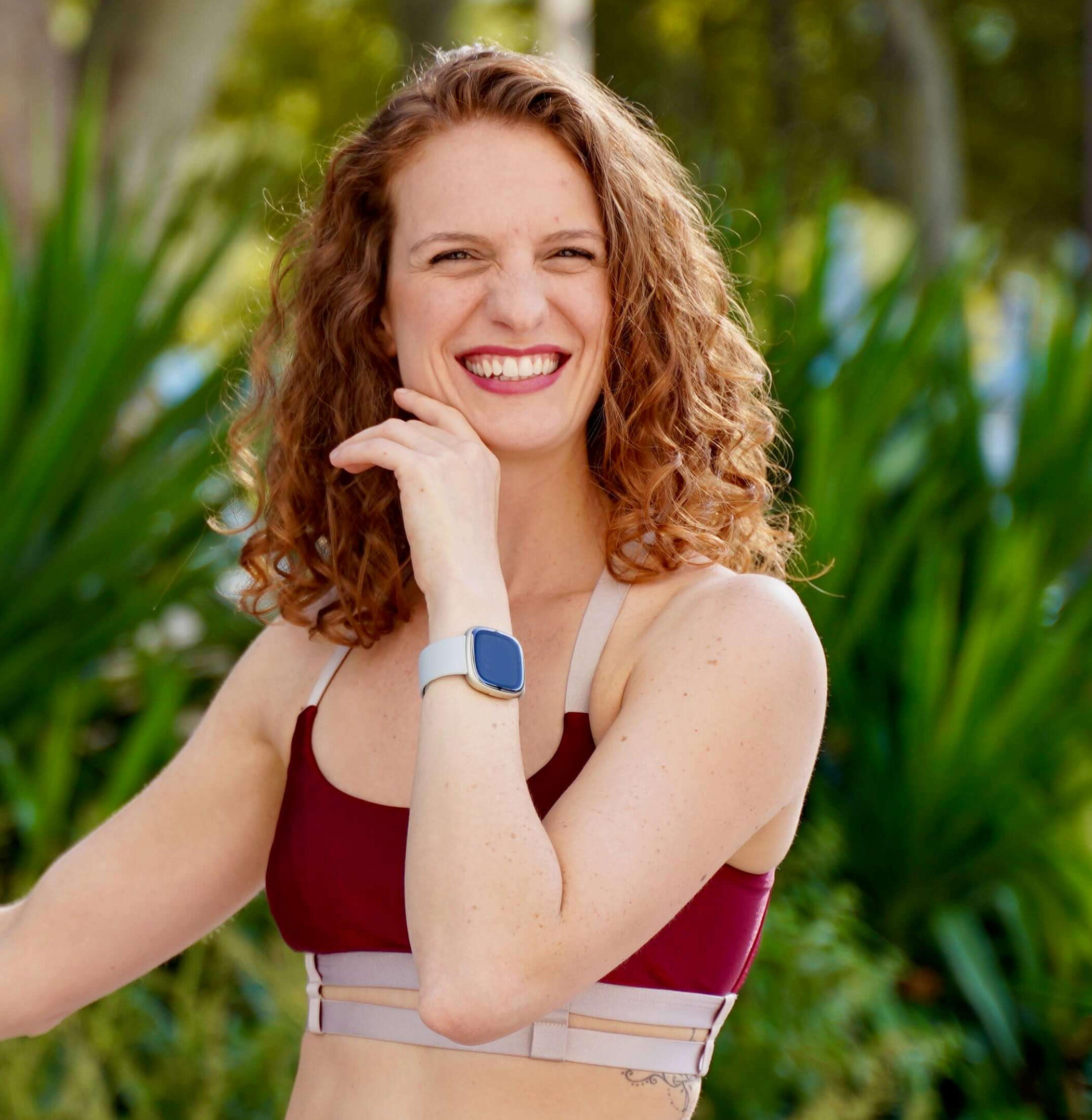 Camila bio Camila smiling in a red top and leafy background